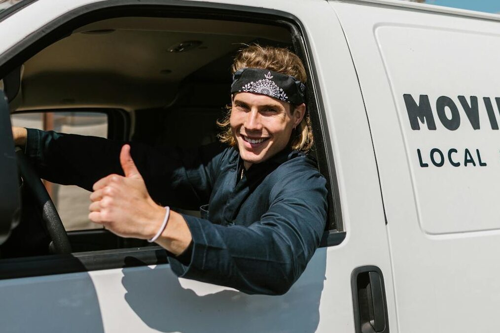 Smiling mover giving thumbs up from a moving company van parked outside.